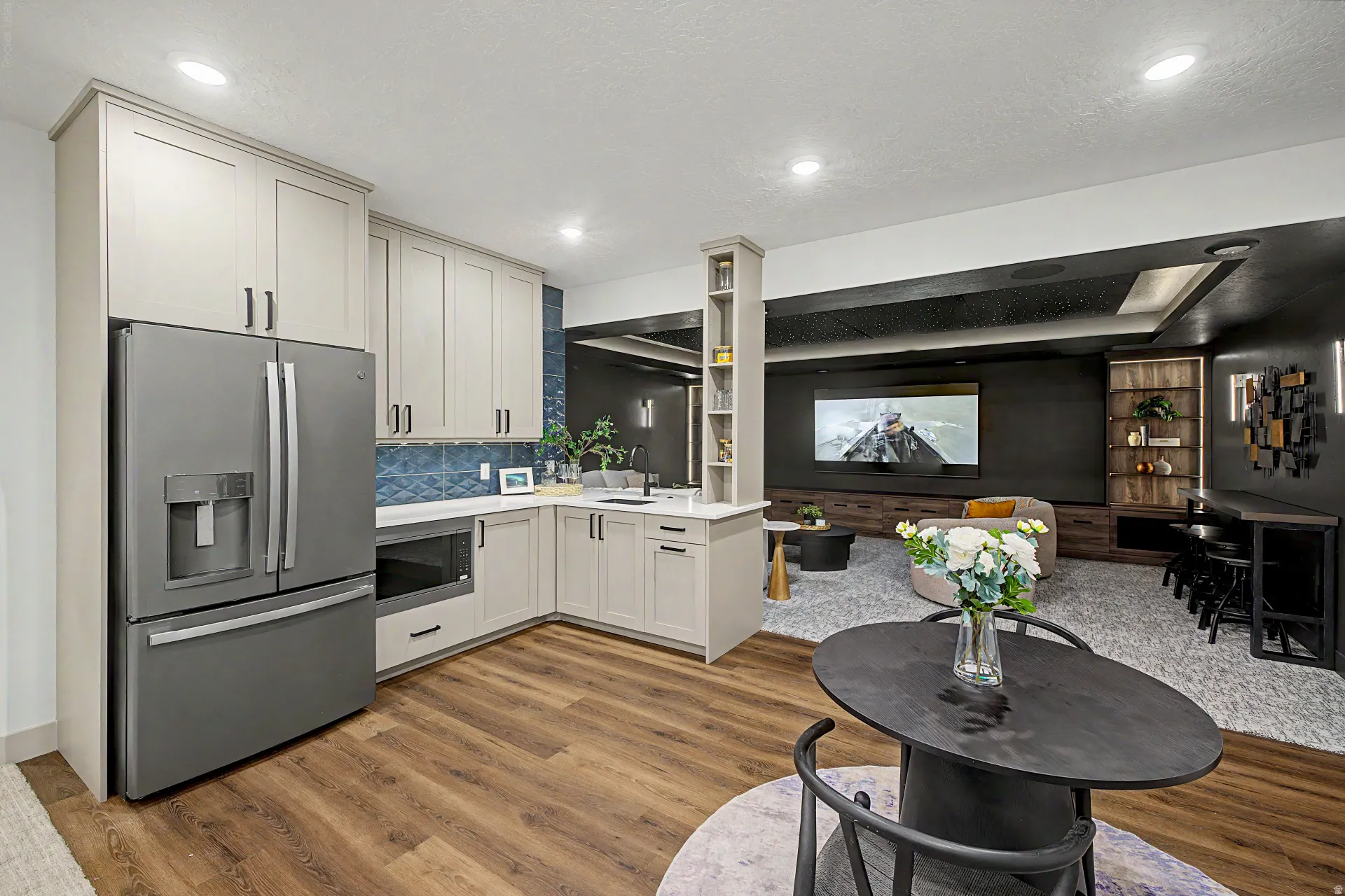 Kitchenette featuring wood-finish flooring, custom cabinetry, a stainless steel refrigerator, white countertops, and a blue tile backsplash