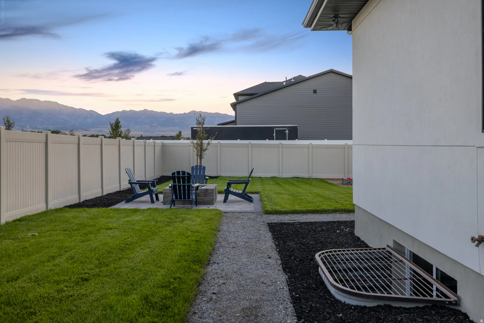 Fenced backyard featuring a fire pit with stone surround, a gravel path, and a grass lawn