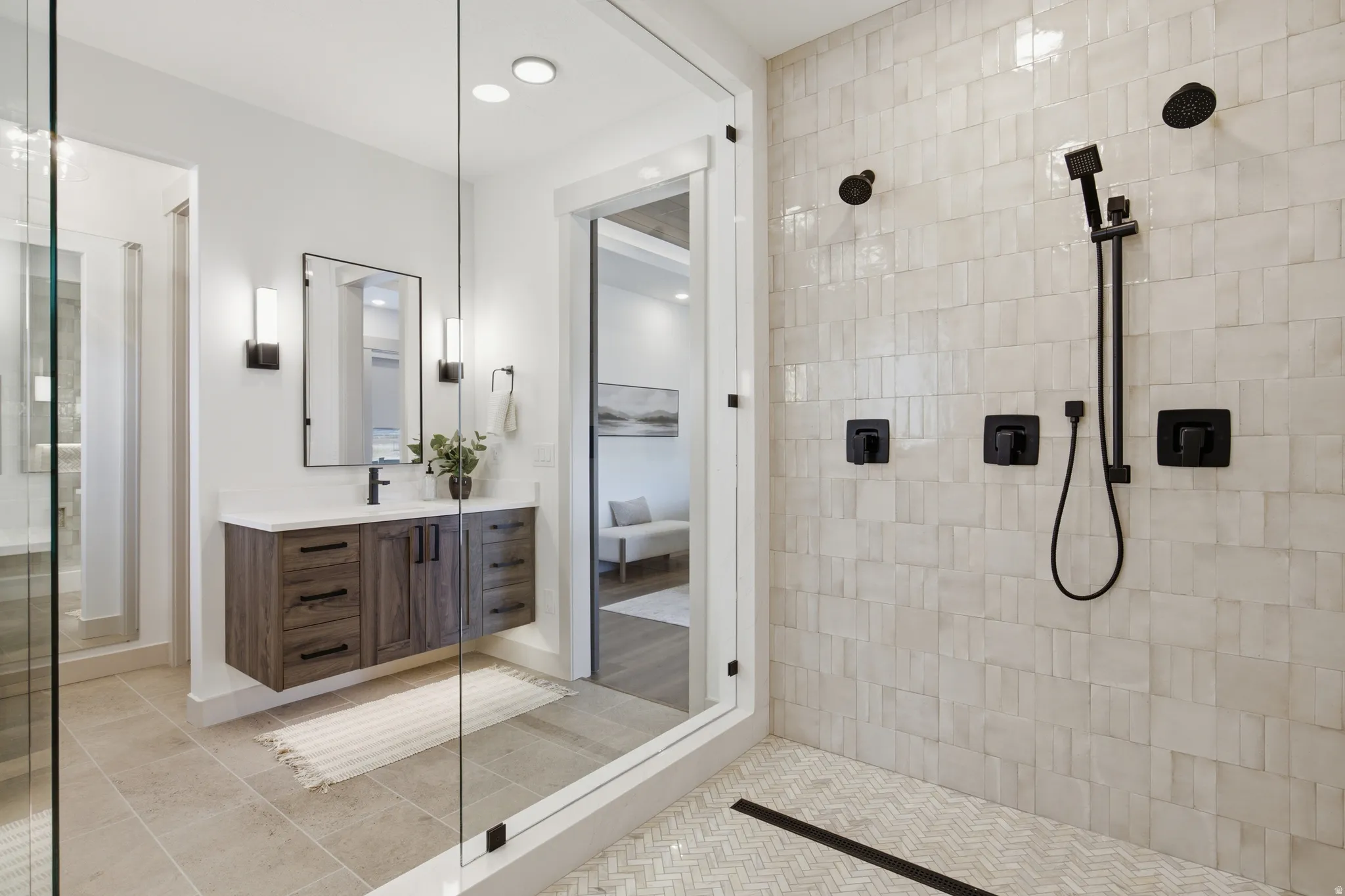 Walk-in shower with textured tile surround and matte black fixtures, complemented by a floating wood-finish vanity with a white countertop and rectangular mirror