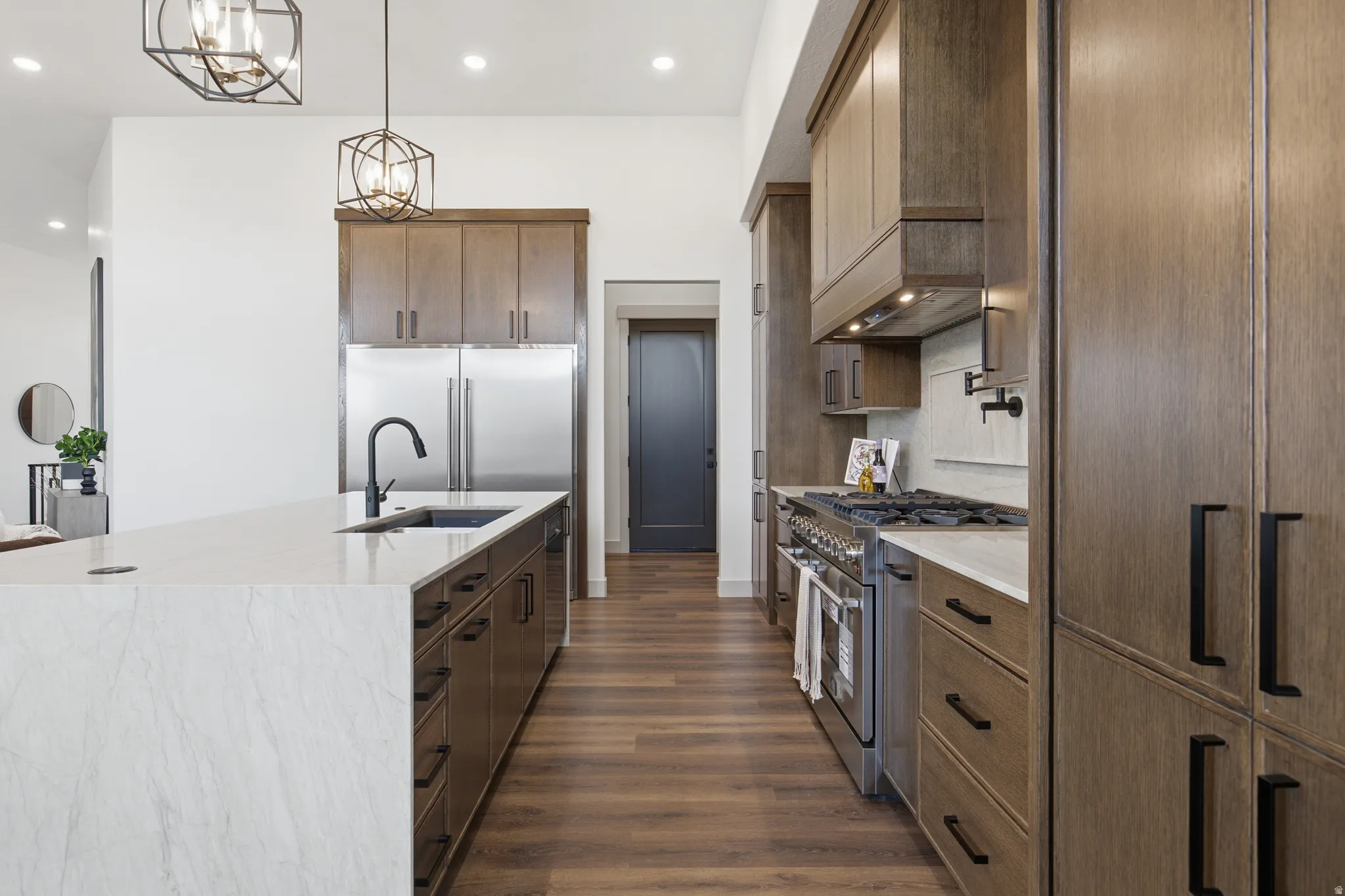 Modern kitchen featuring a large island with a white countertop and undermount sink, rich wood-finish cabinetry, stainless steel appliances, and wood-finish flooring