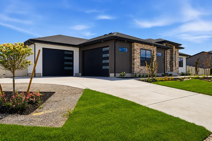 Contemporary single-story residence showcasing a multi-textured facade with stone accents, dark vertical siding, and crisp white panels