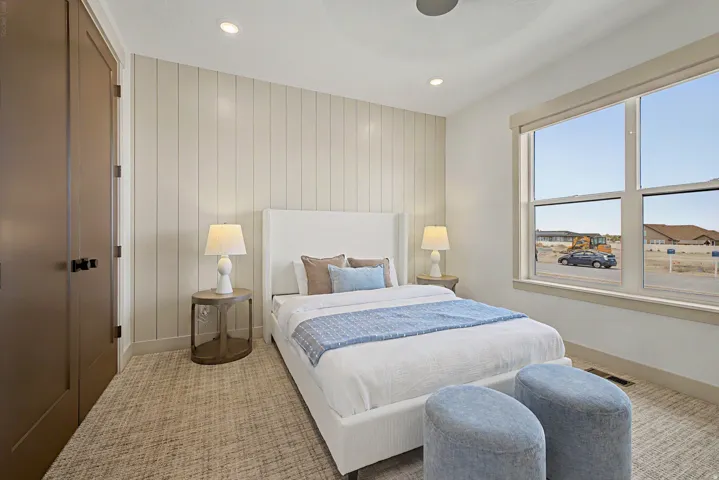 Bedroom featuring a prominent window, neutral-toned plank accent wall, and patterned carpeting