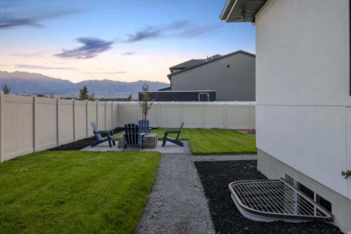Fenced backyard featuring a fire pit with stone surround, a gravel path, and a grass lawn