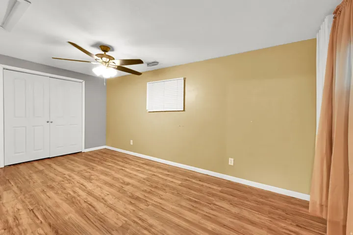Wood-finish flooring, ceiling fan with integrated lighting, wall-mounted window, and bi-fold closet doors