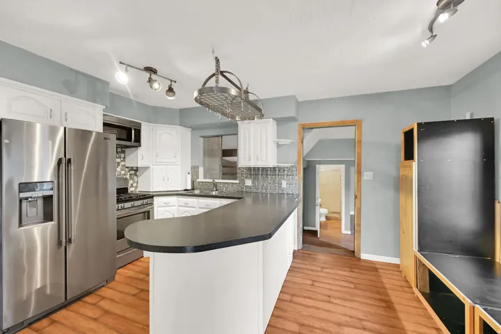 Kitchen featuring wood-finish flooring, white cabinetry, stainless steel appliances, a pot rack, and a peninsula countertop