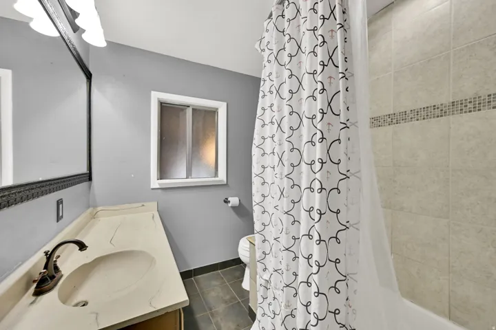 Bathroom featuring a window, vanity with integrated sink, bronze-finish faucet, and tiled shower with mosaic accent