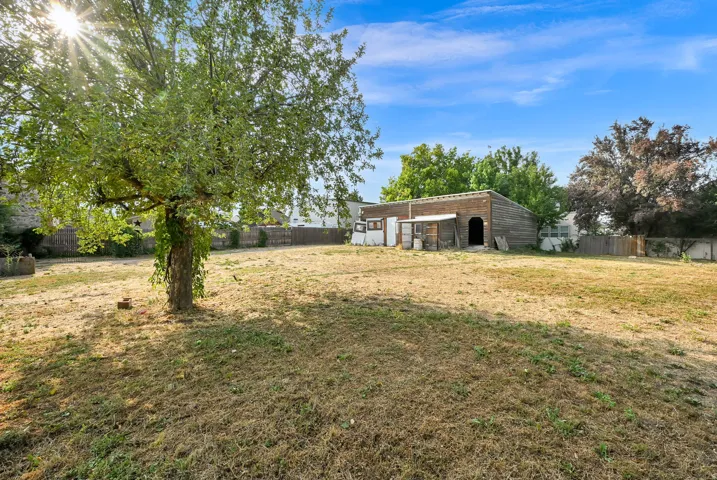 Expansive outdoor space featuring a mature tree, a detached structure with a brick facade, and a fenced perimeter