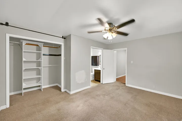 Carpeted flooring, ceiling fan with integrated lighting, and a built-in closet organization system