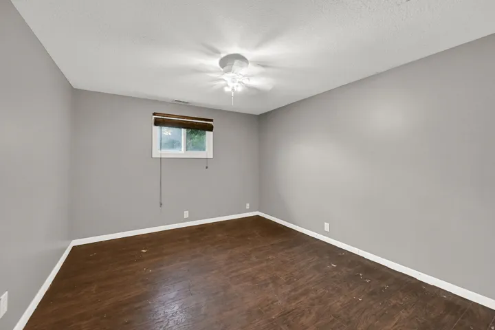 Wood-finish flooring, neutral gray walls, and a white ceiling fan with integrated lighting