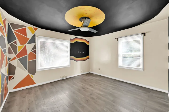 Wood-finish flooring, two windows with blinds, and a ceiling fan with a prominent ceiling medallion