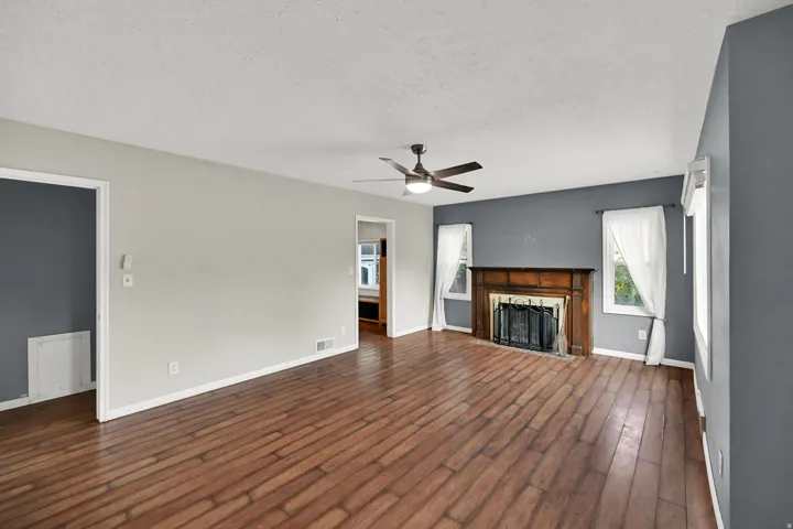 Wood-finish flooring, a ceiling fan with integrated lighting, a fireplace with a wood mantel, and multiple windows