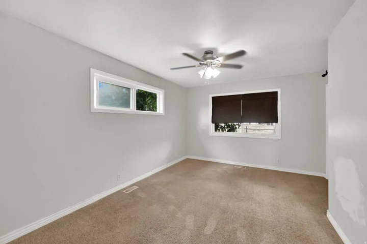 Neutral tone wall paint, dual windows, ceiling fan with integrated lighting, and carpeted flooring