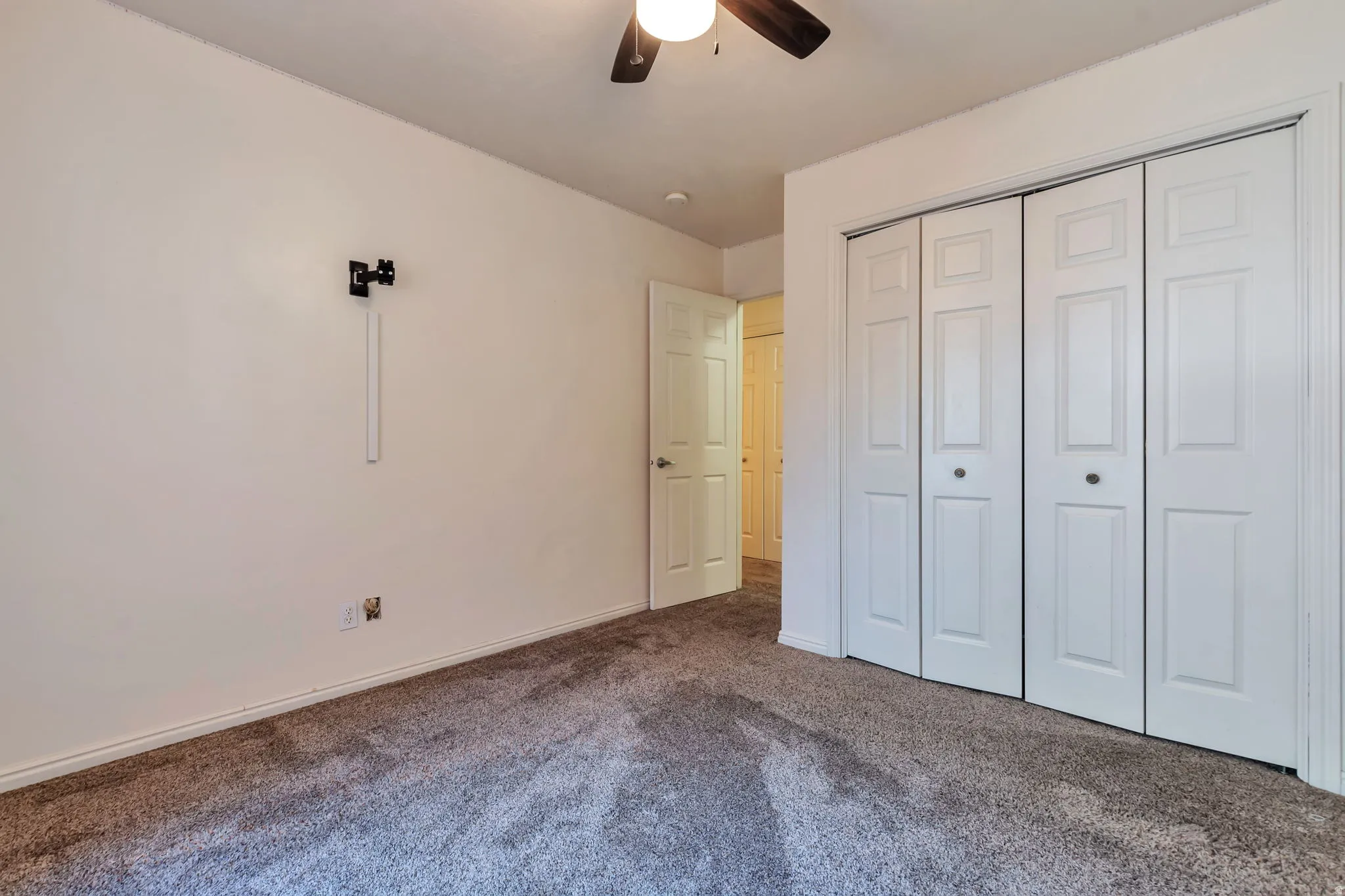 Carpeted room featuring a ceiling fan, white bi-fold closet doors, and white baseboards
