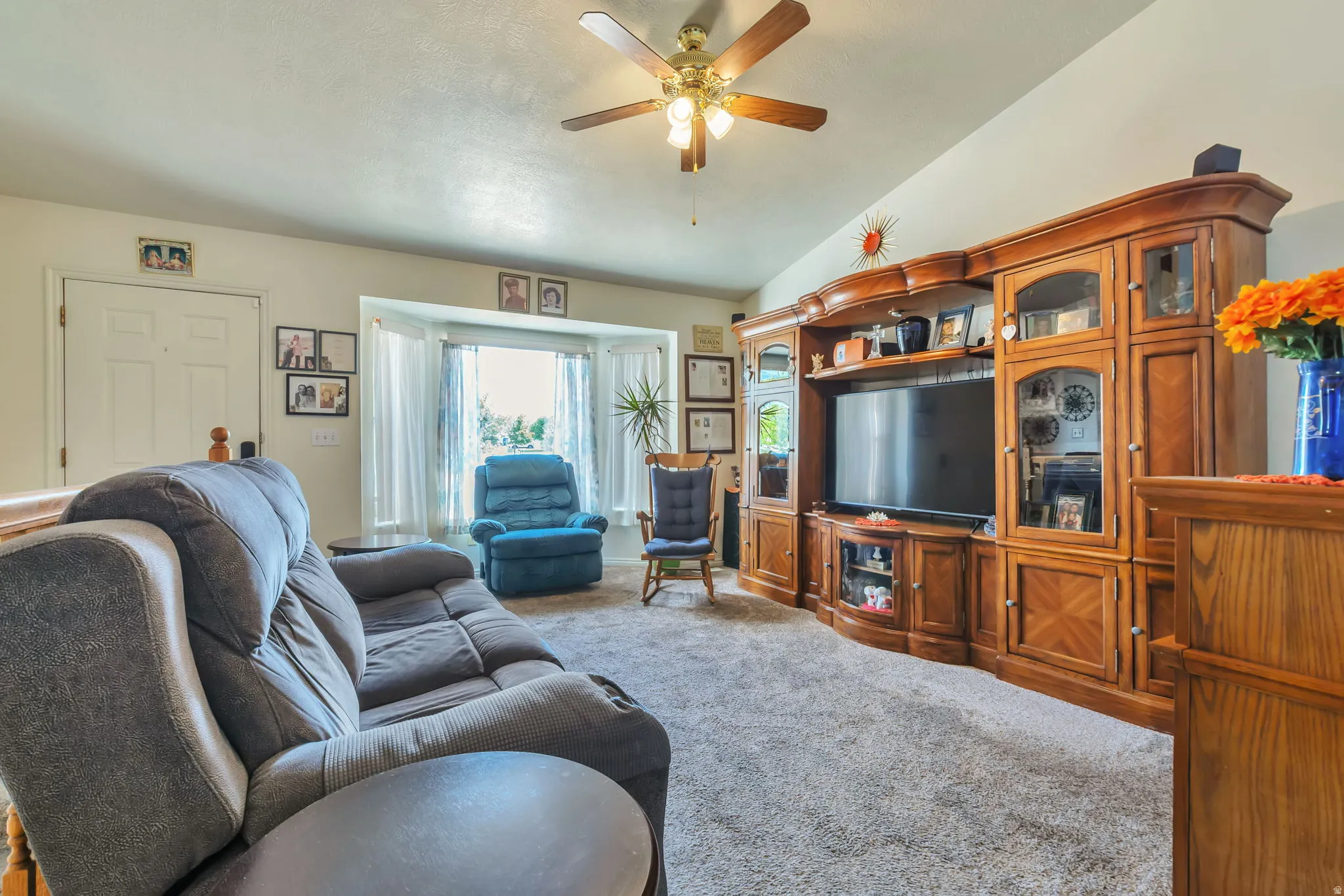 Spacious living area featuring vaulted ceilings, a ceiling fan with integrated lighting, and soft gray carpeting