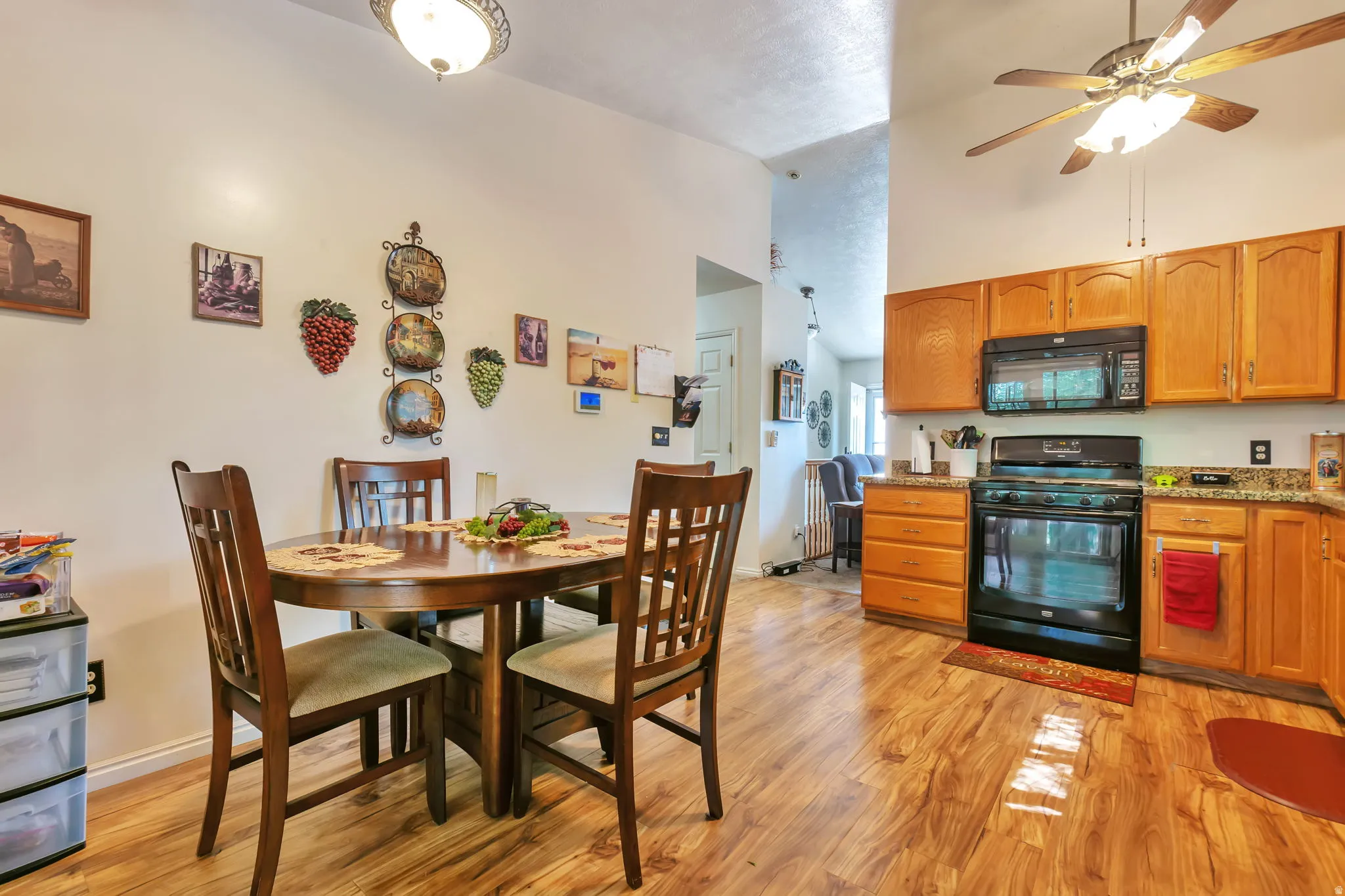 Kitchen featuring wood-finish flooring, oak cabinetry, black appliances, and speckled countertops