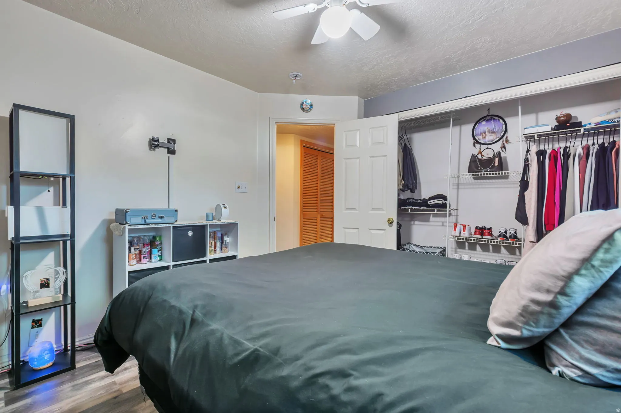 Bedroom featuring wood-finish flooring, a ceiling fan with integrated lighting, and a closet with bifold doors and wire shelving