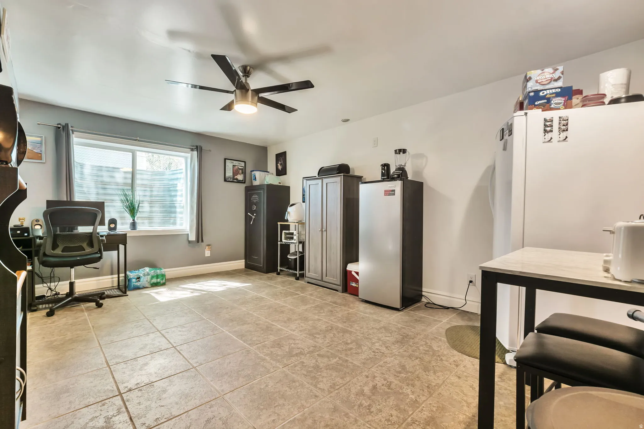 Spacious room featuring neutral tile flooring, a window providing natural light, a ceiling fan, and painted walls