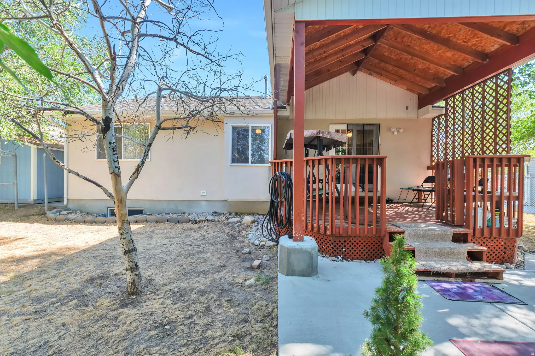 Covered wooden deck featuring a slatted ceiling, lattice privacy screen, and railing