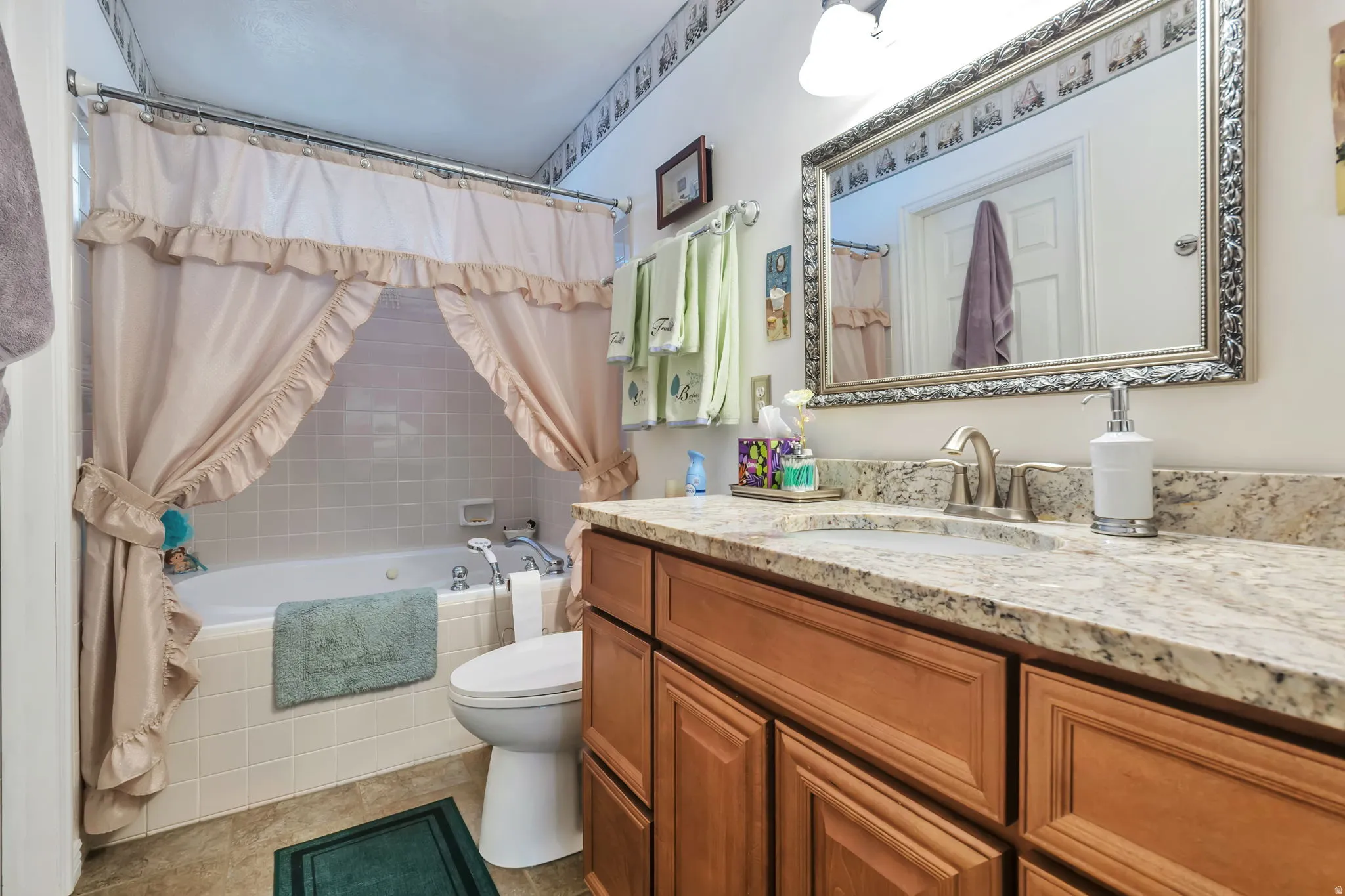 Bathroom featuring a built-in tub with tile surround, a single vanity with stone countertop and integrated sink, wood-finish cabinetry, and a framed mirror