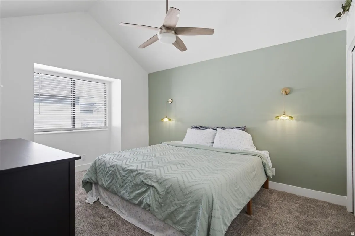 Vaulted ceiling bedroom featuring a ceiling fan, recessed window with blinds, two wall-mounted sconces, and neutral carpet