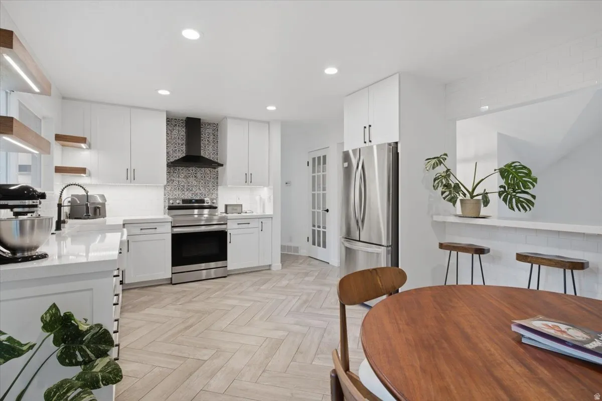Contemporary kitchen featuring white cabinetry, stainless steel appliances, herringbone wood-finish flooring, recessed lighting, and a patterned tile backsplash