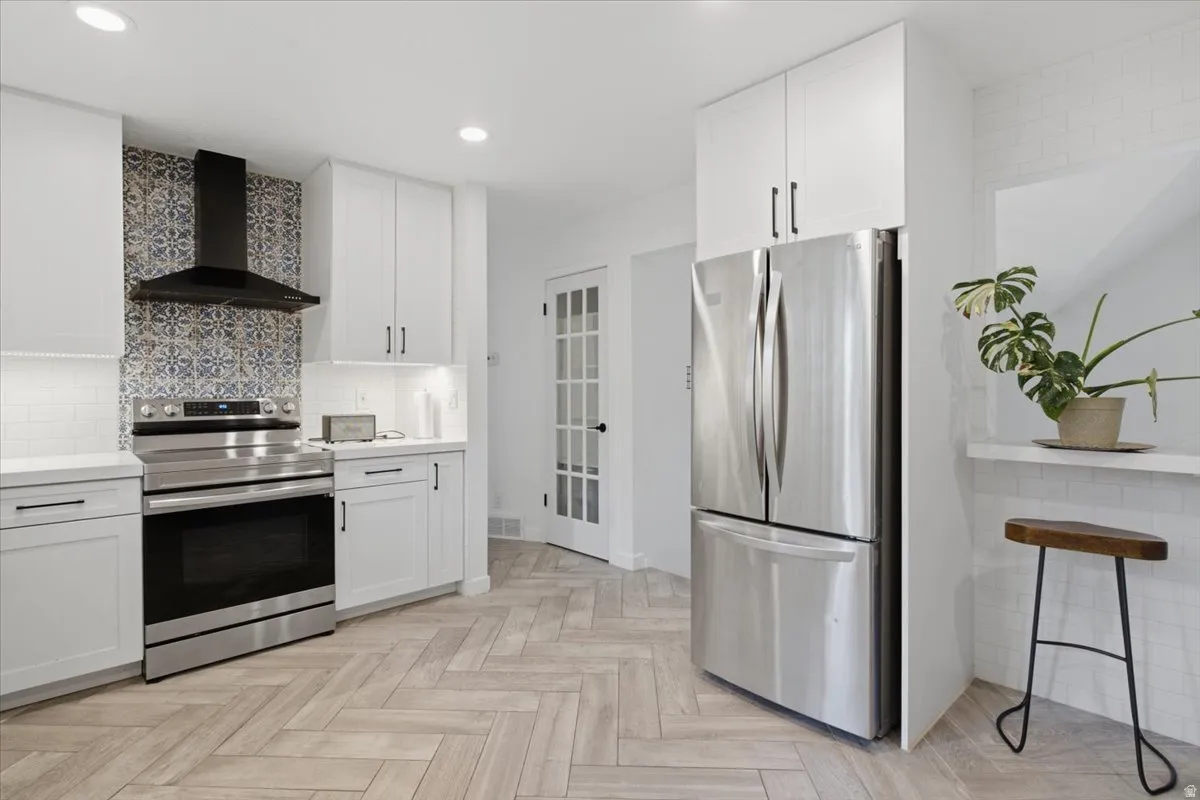 Modern kitchen featuring white cabinetry, stainless steel appliances, and wood-finish flooring in a herringbone pattern