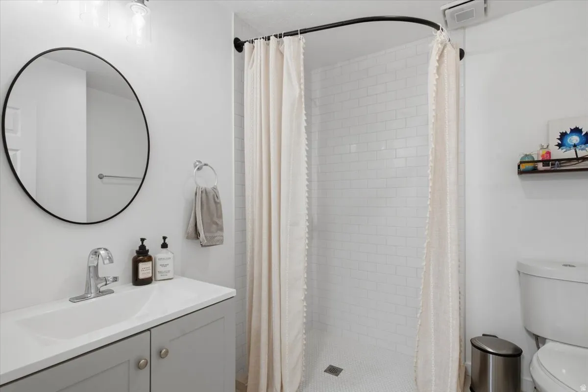 Bathroom featuring a vanity with a white countertop and undermount sink, a circular black-framed mirror, a subway-tiled shower, and mosaic tile flooring