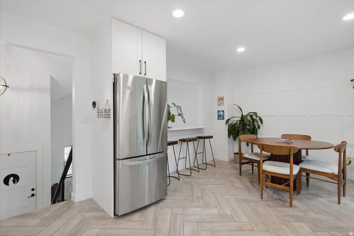 Open-concept living area featuring herringbone-pattern wood-finish flooring, a built-in stainless steel refrigerator, recessed lighting, and a paneled accent wall