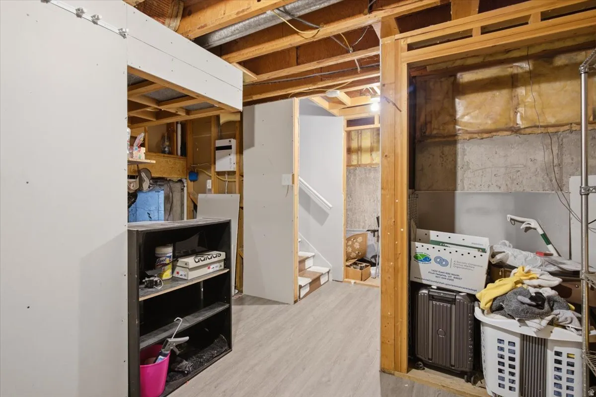 Unfinished basement featuring exposed wood framing, concrete walls, partial drywall installations, and wood-finish flooring