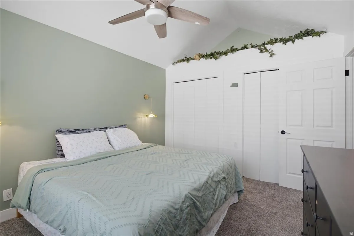 Bedroom featuring a vaulted ceiling with a ceiling fan, wall-mounted sconces, and neutral wall paint