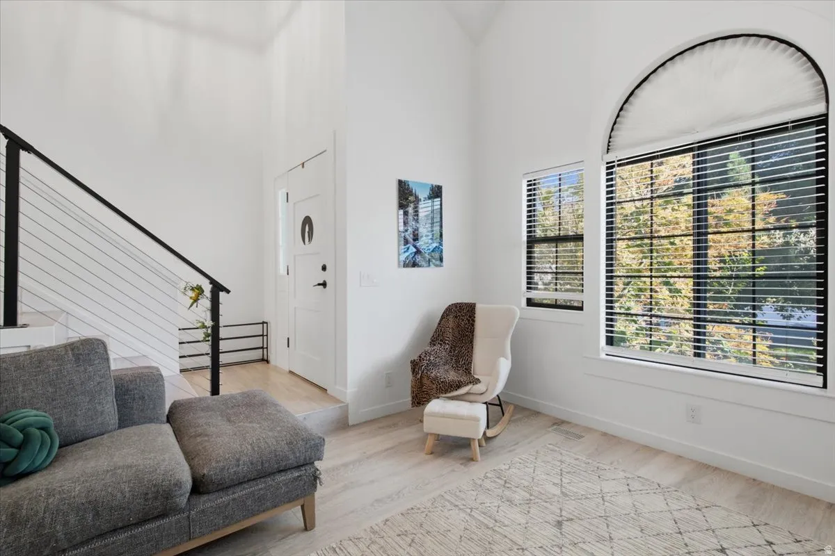 Bright interior space featuring a large arched window with horizontal blinds, light wood-finish flooring, a contemporary cable railing system, a white panel door, and high ceilings