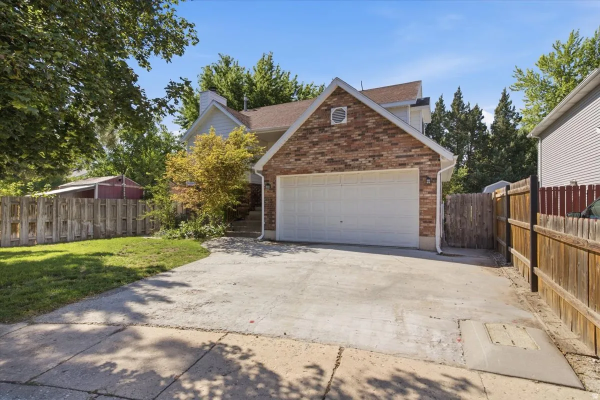 Brick and siding exterior featuring an integrated two-car garage with a white door, a concrete driveway, a wooden privacy fence, and mature landscaping
