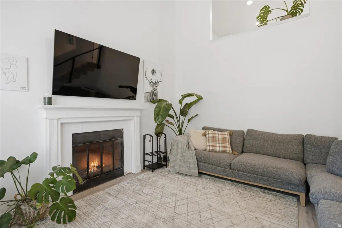 Living area featuring a white mantel fireplace, a large wall-mounted television, a high ceiling, and a large window opening