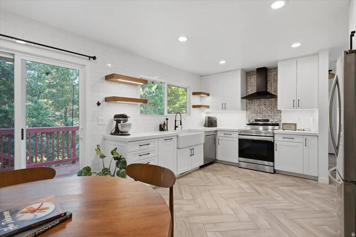 Kitchen featuring white shaker cabinetry, stainless steel appliances, a farmhouse-style sink, and herringbone wood-finish flooring