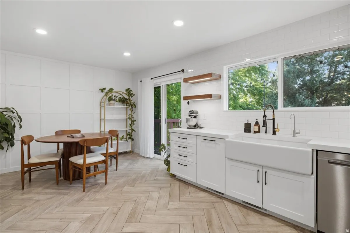 Kitchen and dining area featuring herringbone wood-finish flooring, white flat-panel cabinetry with black hardware, and a white farmhouse sink