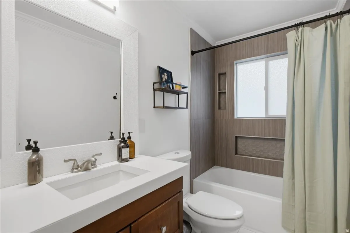 Bathroom featuring a wood-finish vanity with an integrated sink and brushed nickel faucet, a large framed mirror, and a tiled tub surround with built-in niches