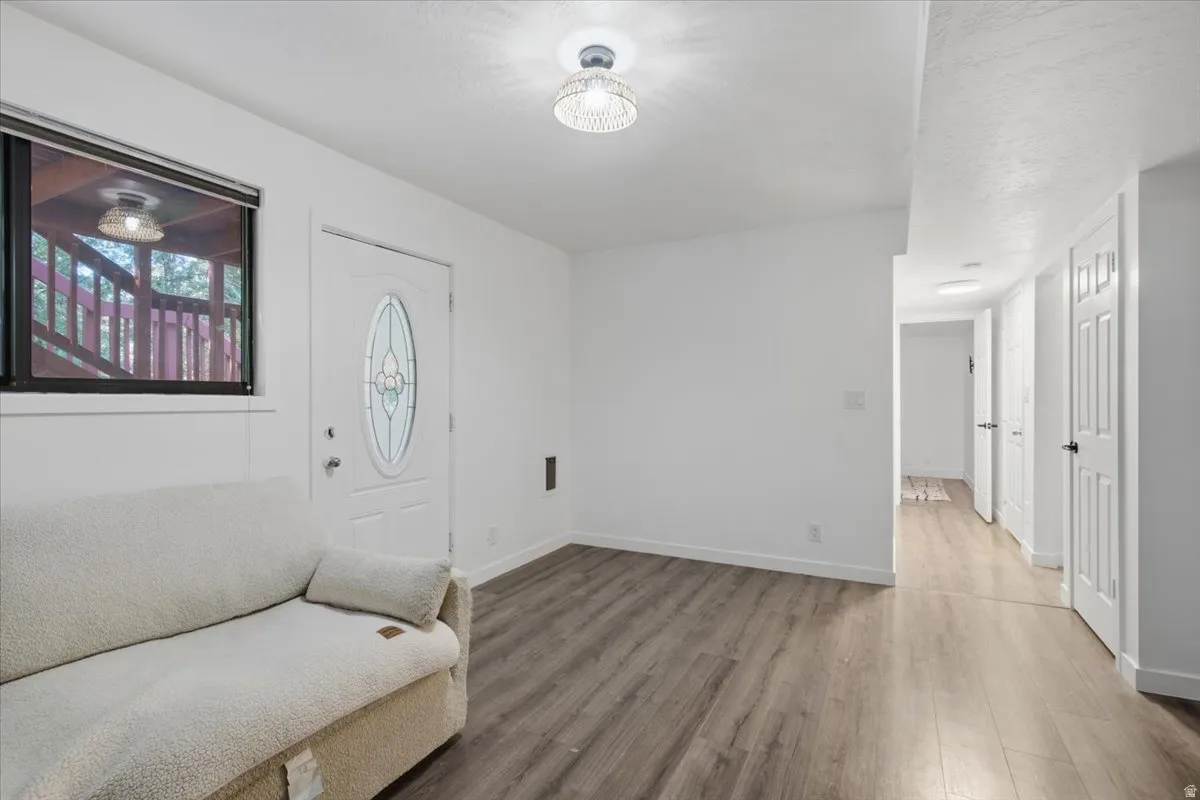 Bright interior featuring wood-finish flooring, white walls, and a white entry door with decorative glass inlay