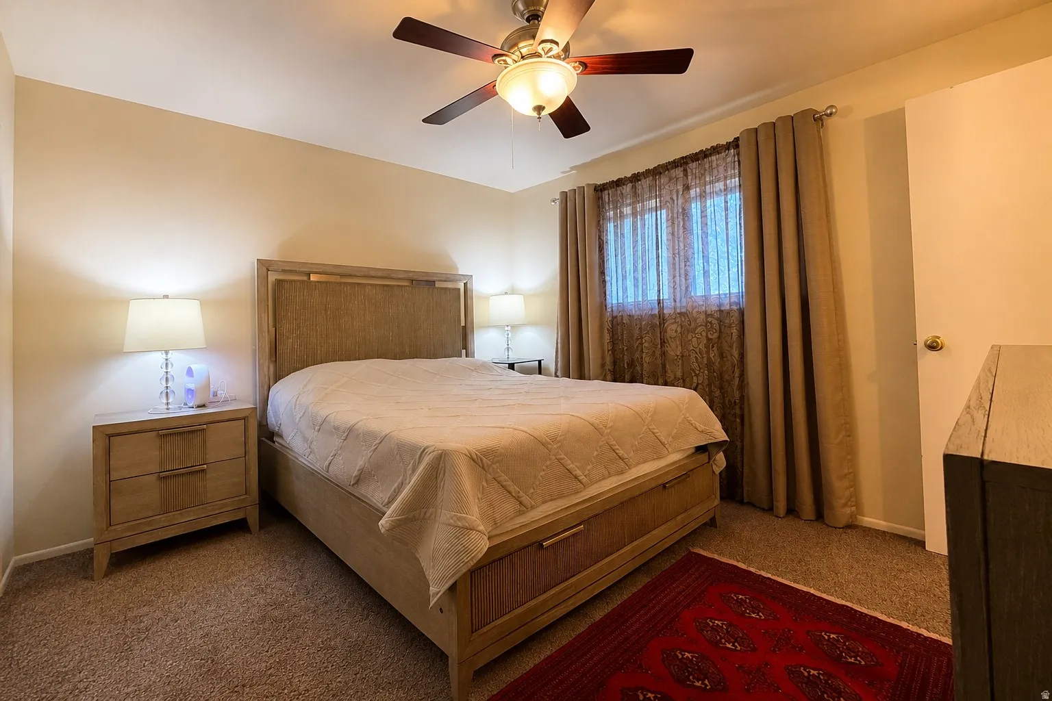 Carpeted interior with a ceiling fan, light-toned walls, and window treatments