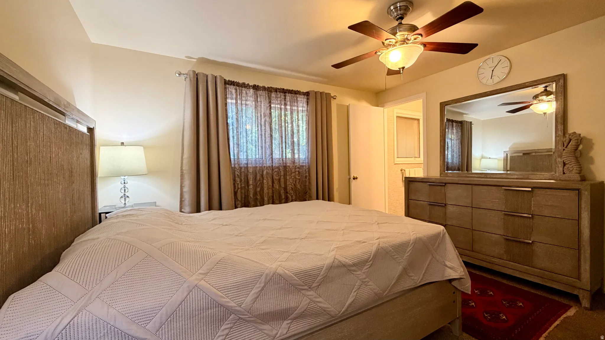 Spacious bedroom featuring light-colored walls, a ceiling fan with integrated lighting, and a window with both sheer and blackout curtains