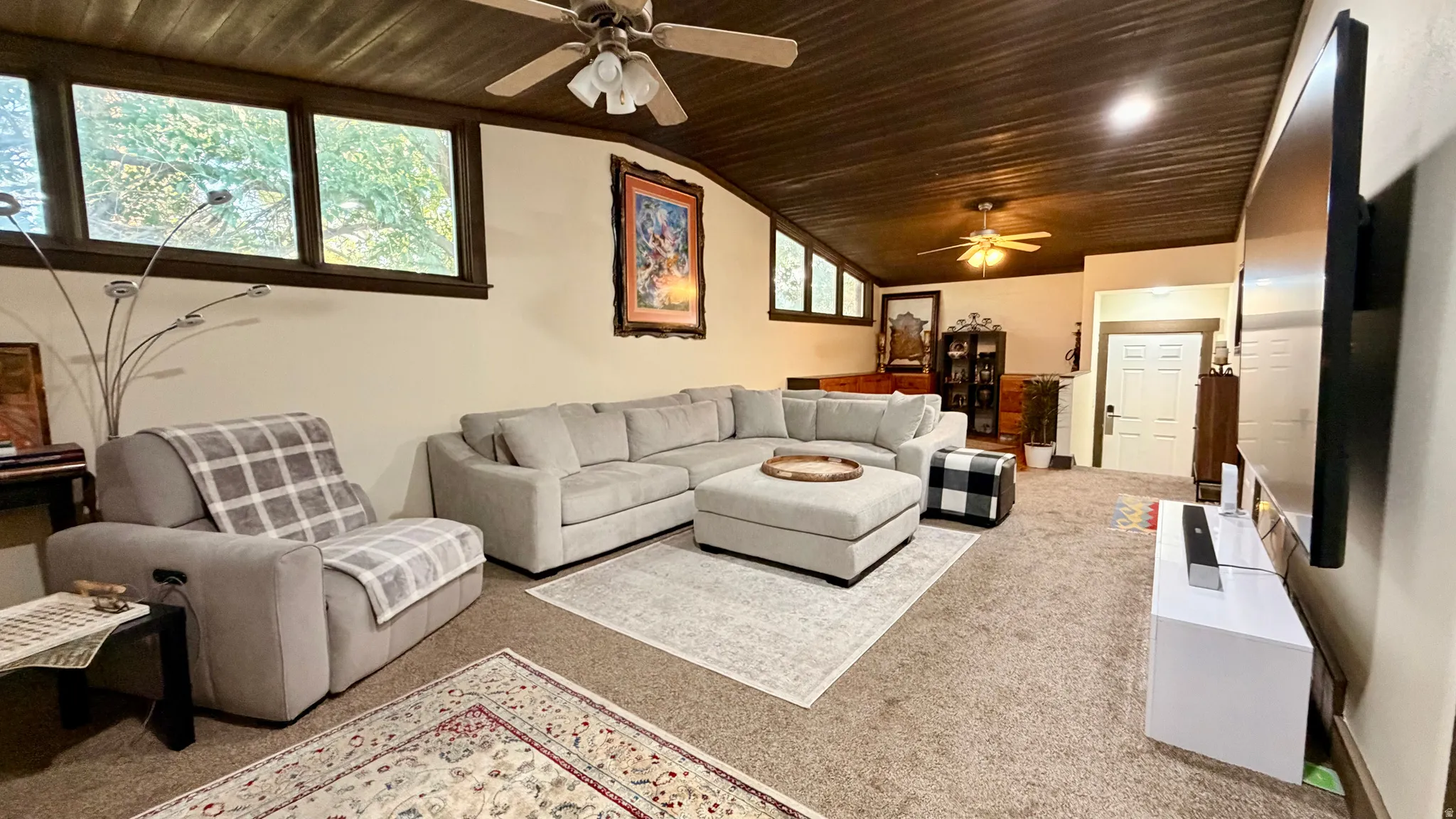 Spacious living area featuring a rich wood-paneled ceiling, large multi-paned windows, and wall-to-wall carpeting