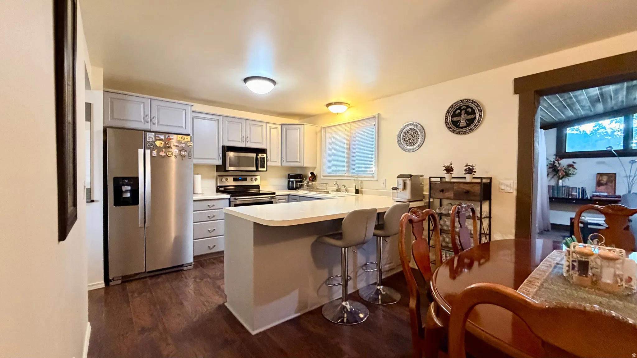 Open-concept kitchen featuring wood-finish flooring, light gray cabinetry, stainless steel appliances, and a central island with countertop seating
