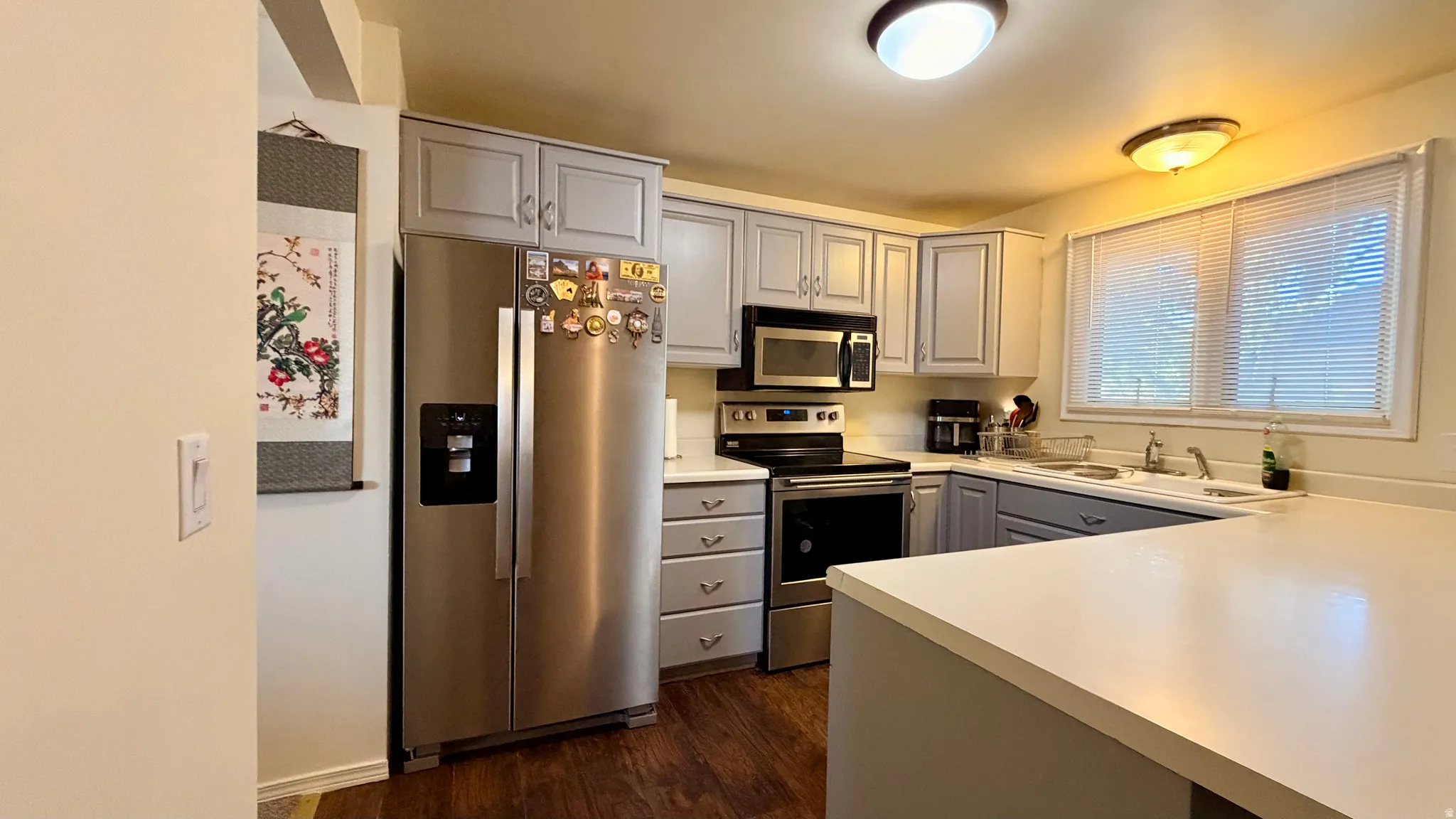 U-shaped kitchen featuring wood-finish flooring, light gray cabinetry, light countertops, and stainless steel appliances including a refrigerator, range, and microwave