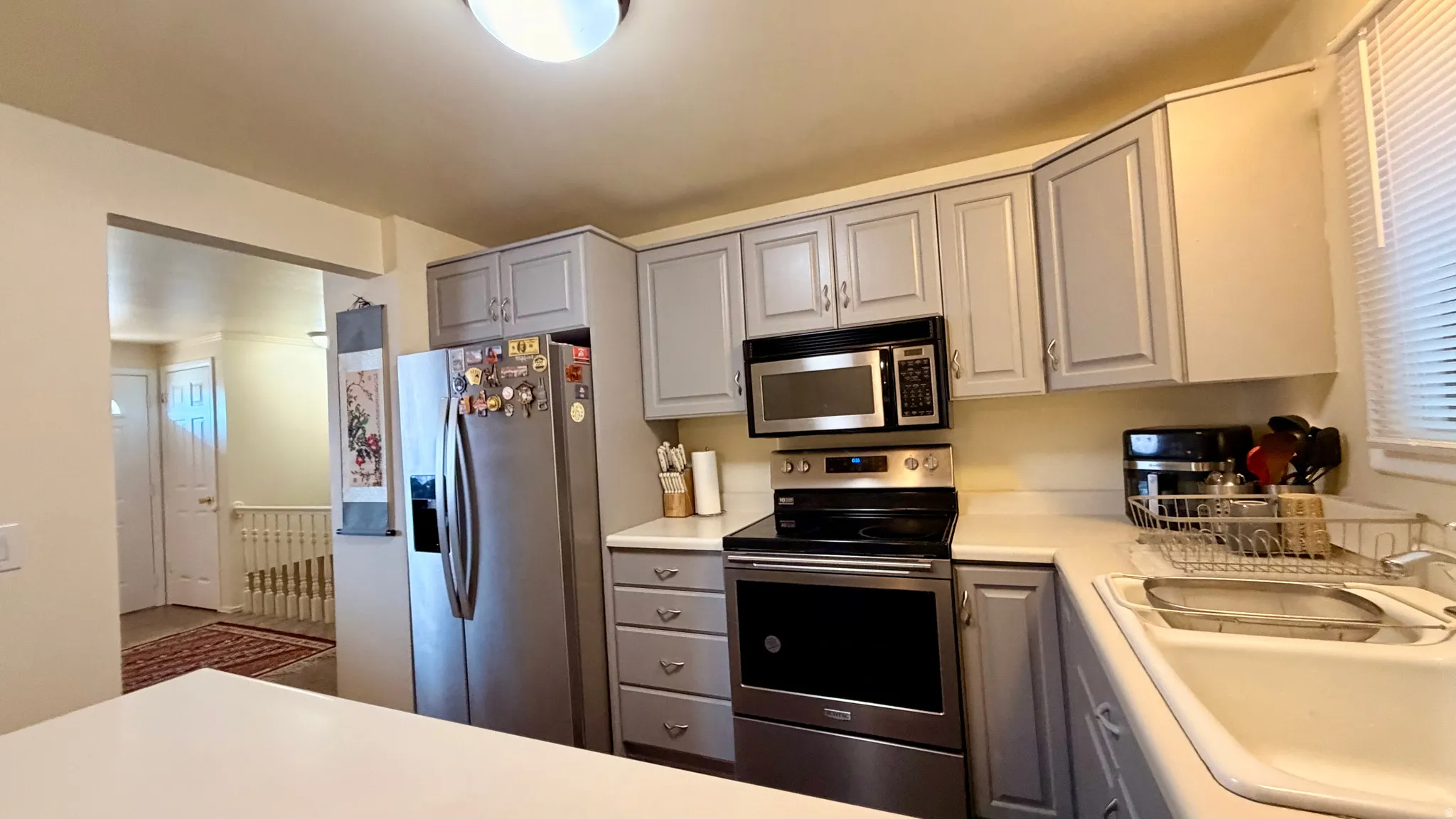 Kitchen featuring light gray cabinetry, stainless steel appliances, a white sink, and white countertops