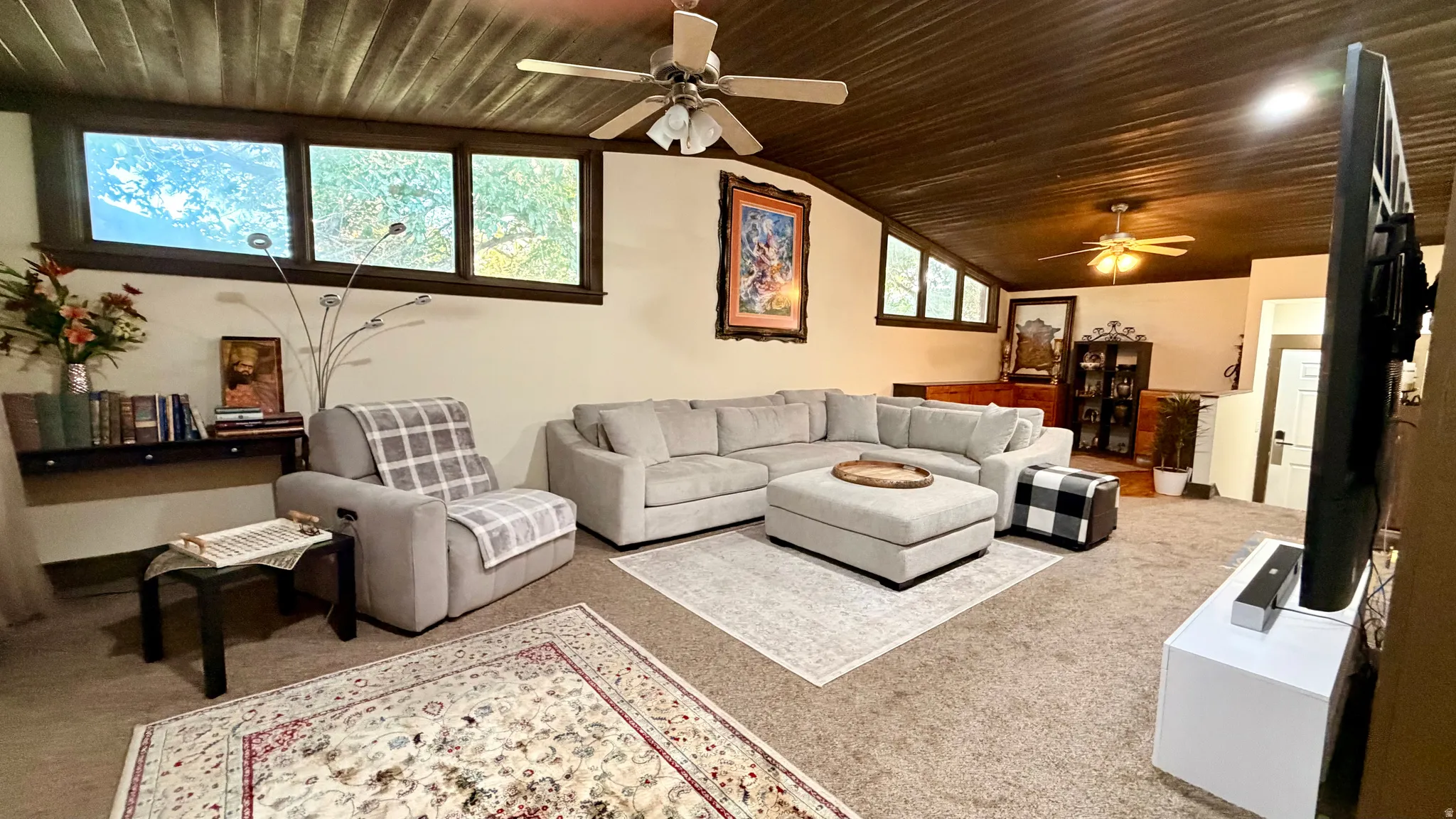 Spacious recreation room featuring a textured wood ceiling, multiple ceiling fans, and a combination of carpet and area rugs