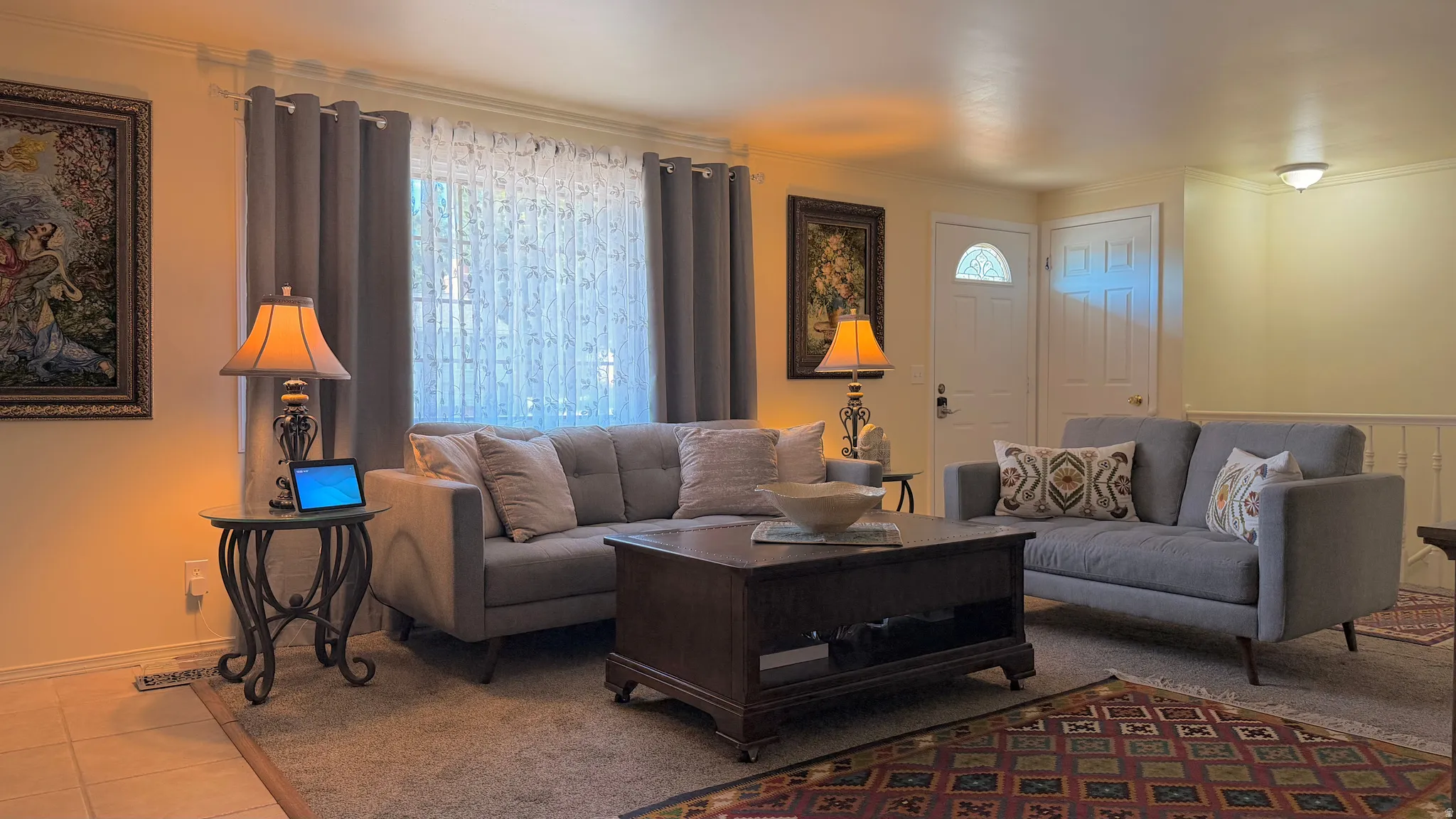 Living area featuring a large window with sheer and solid privacy drapes, carpeted flooring, and a white paneled entry door with an arched glass insert