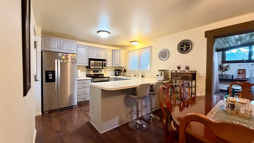 Open-concept kitchen featuring wood-finish flooring, light gray cabinetry, stainless steel appliances, and a central island with countertop seating