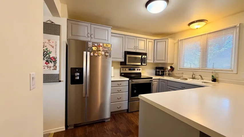 U-shaped kitchen featuring wood-finish flooring, light gray cabinetry, light countertops, and stainless steel appliances including a refrigerator, range, and microwave