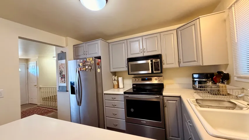 Kitchen featuring light gray cabinetry, stainless steel appliances, a white sink, and white countertops