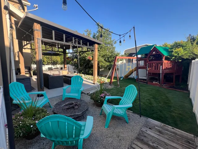 Outdoor living space featuring a covered patio with built-in overhead lighting, a stone fire pit, and a manicured lawn area