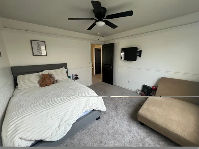 Room featuring light gray carpeting, crisp white walls with wainscoting, and a ceiling fan with integrated lighting